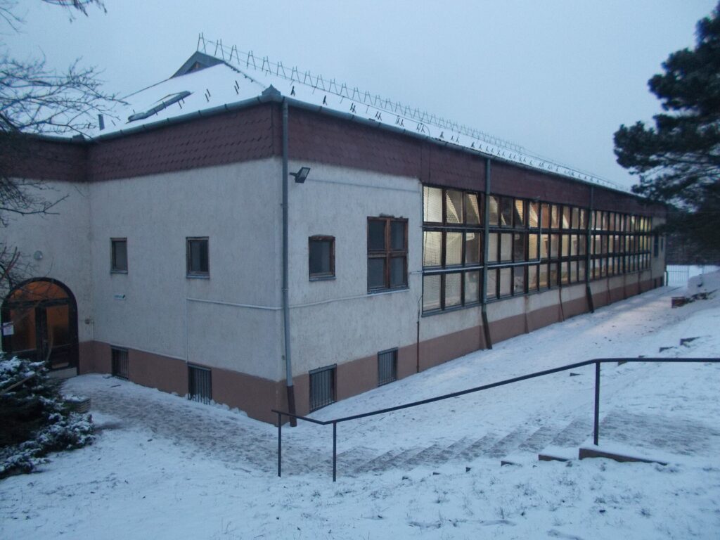 A plain indoor sports hall with court markings and stacked benches along one wall