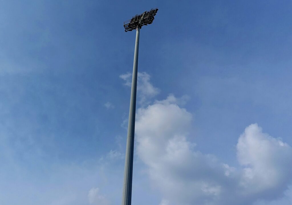 A floodlight pylon rising above a stadium roof against an early evening sky