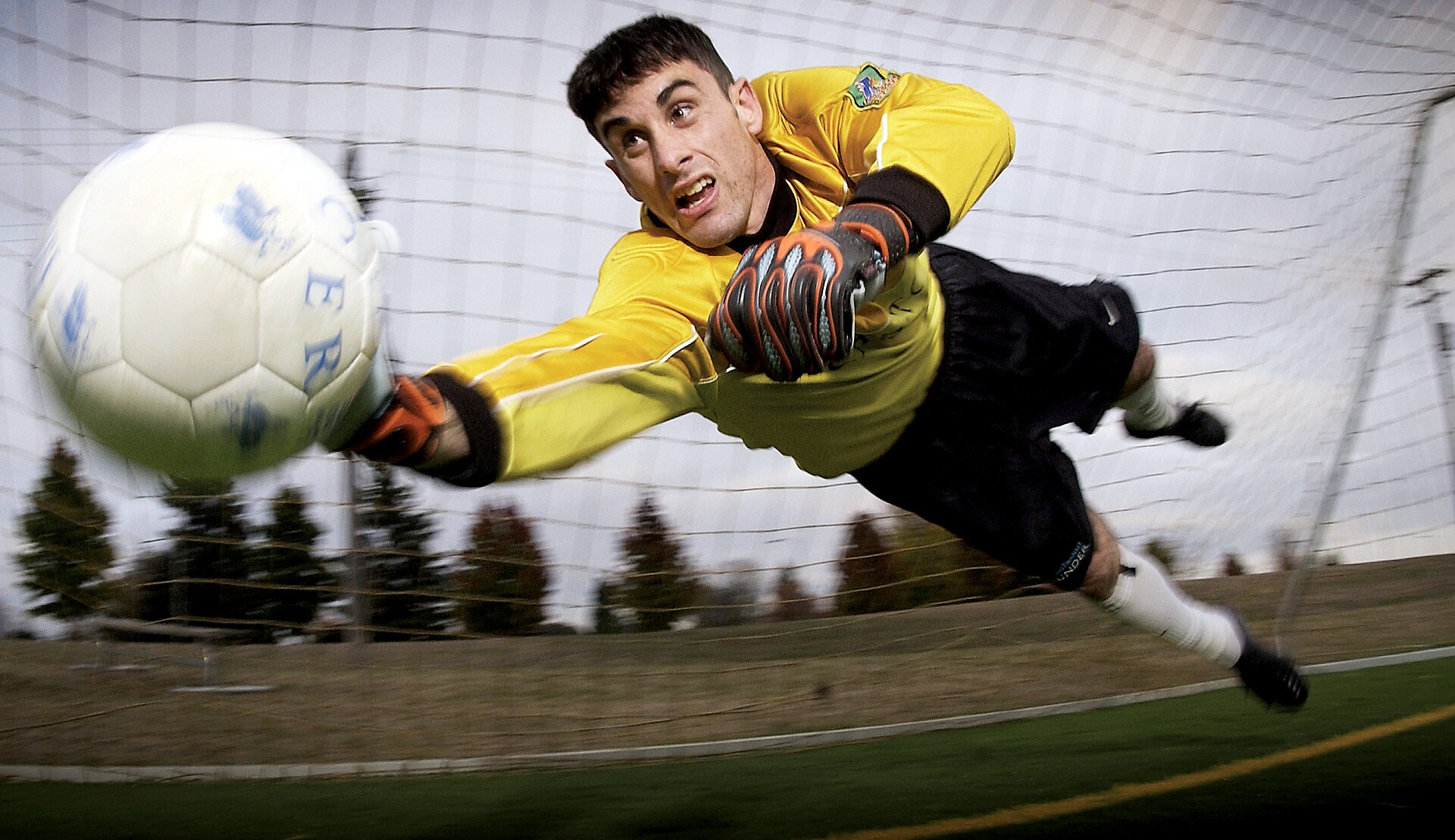 A goalkeeper stretching sideways through the air to reach a shot in front of the goal