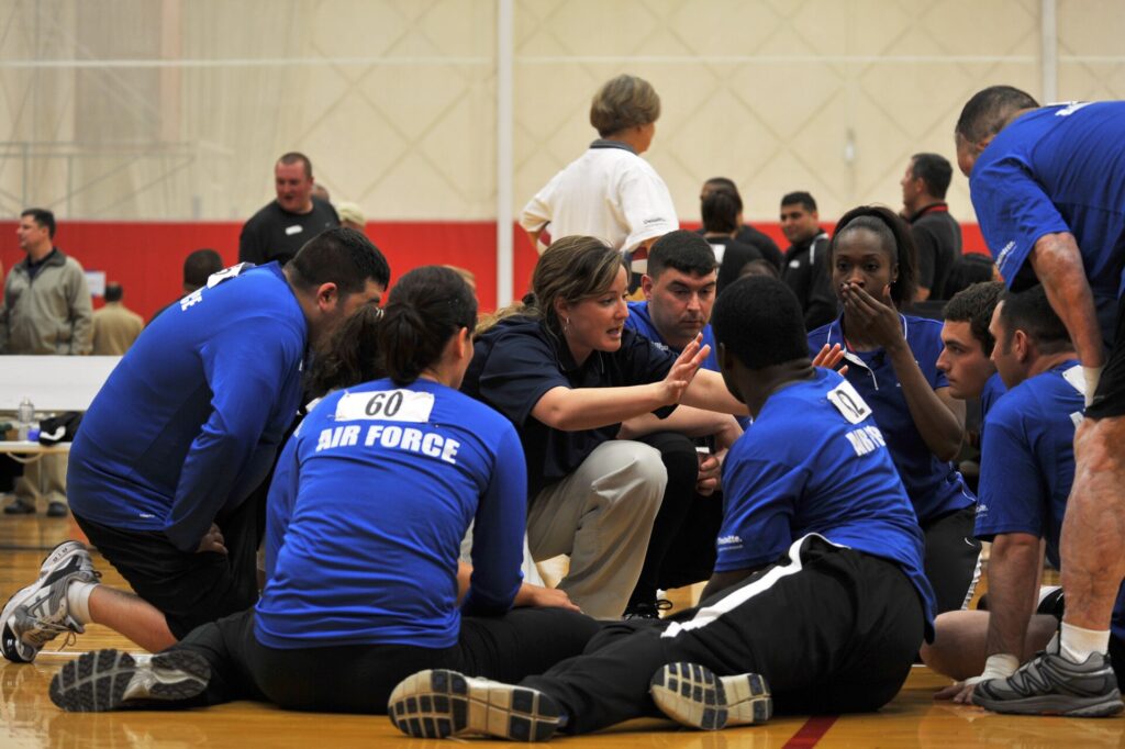 Six players gathered in a circle on an indoor court between rallies