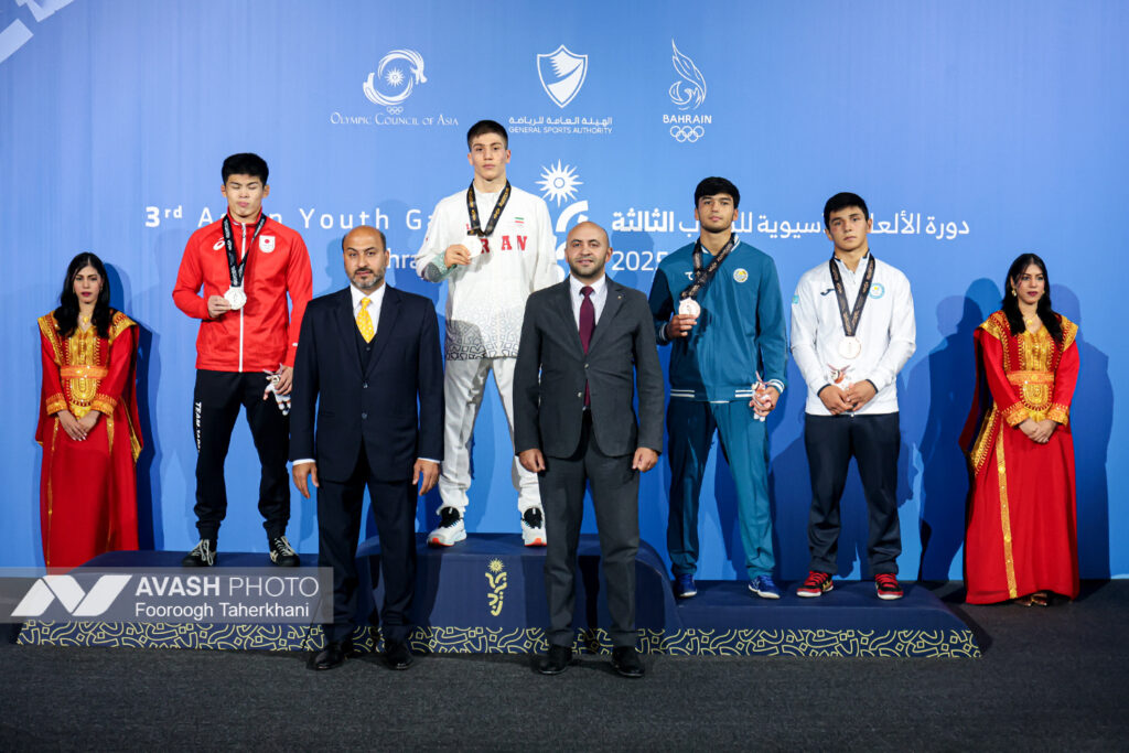 Young wrestlers practising holds on a mat while a coach watches from the side