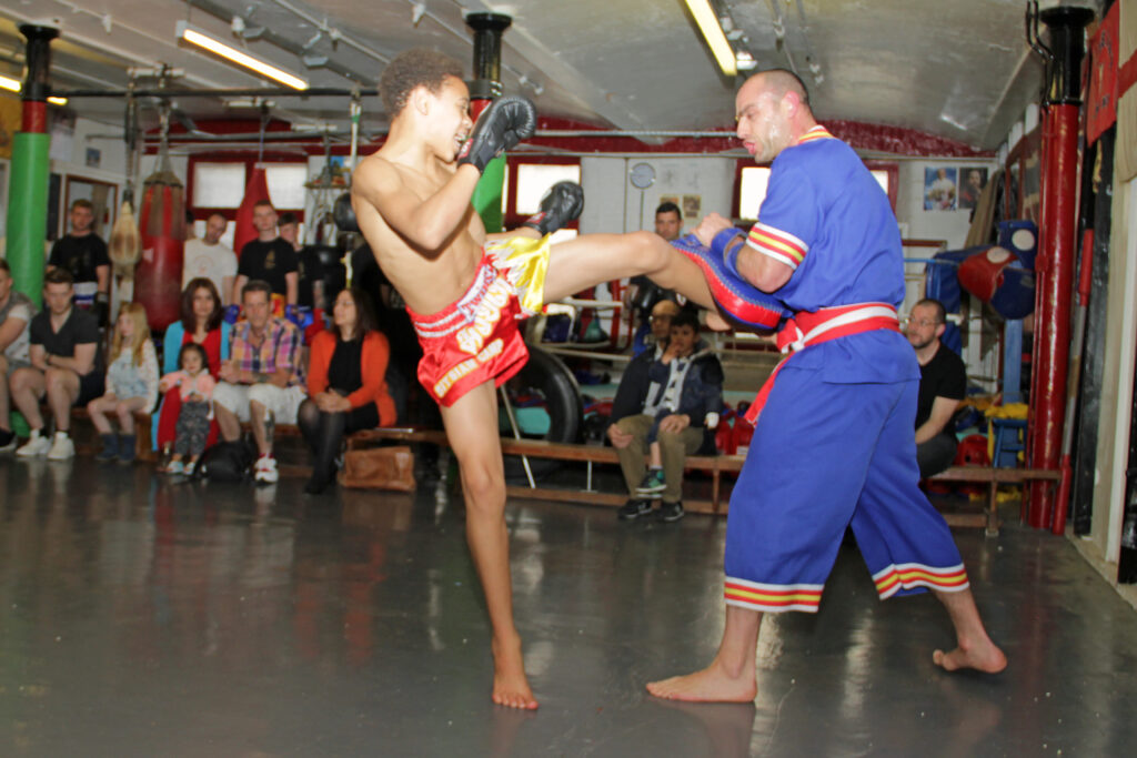 A coach holding a rectangular kicking pad while a student prepares to strike it