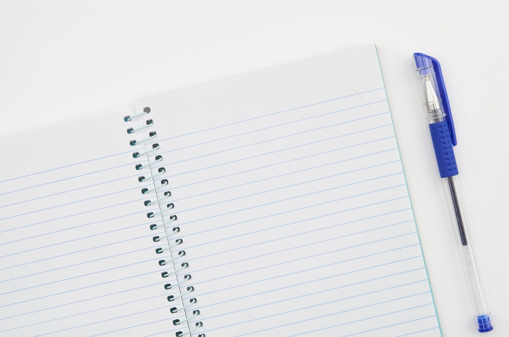 An open notebook with handwritten columns of figures beside a pen on a table