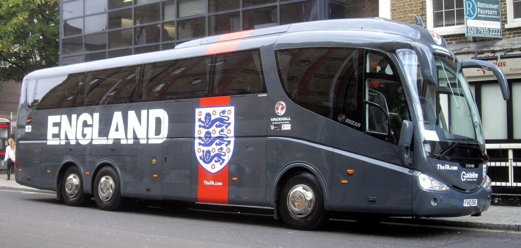 A long-distance coach parked outside a sports venue with luggage compartments open