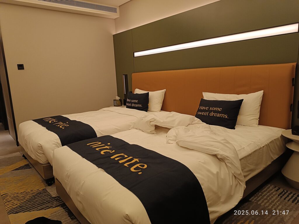 Two made beds in a plain hotel room with curtains drawn against the daylight