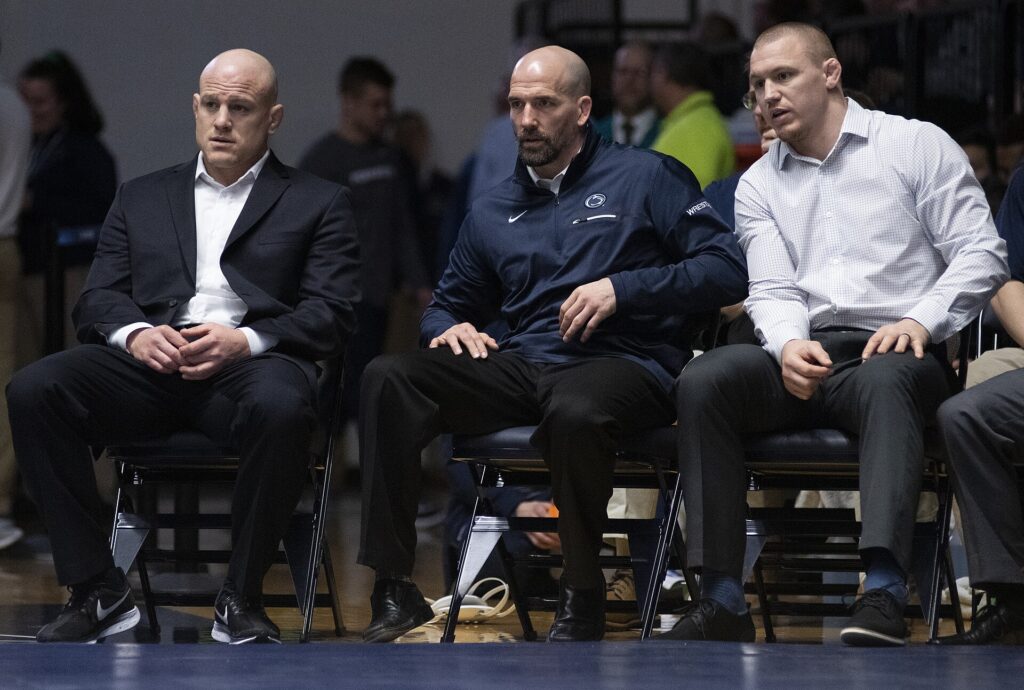 A coach leaning over the edge of the mat calling instructions during a bout