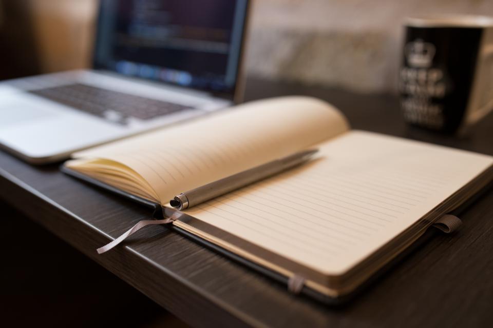 An open notebook with handwritten figures beside a pen and a small calculator