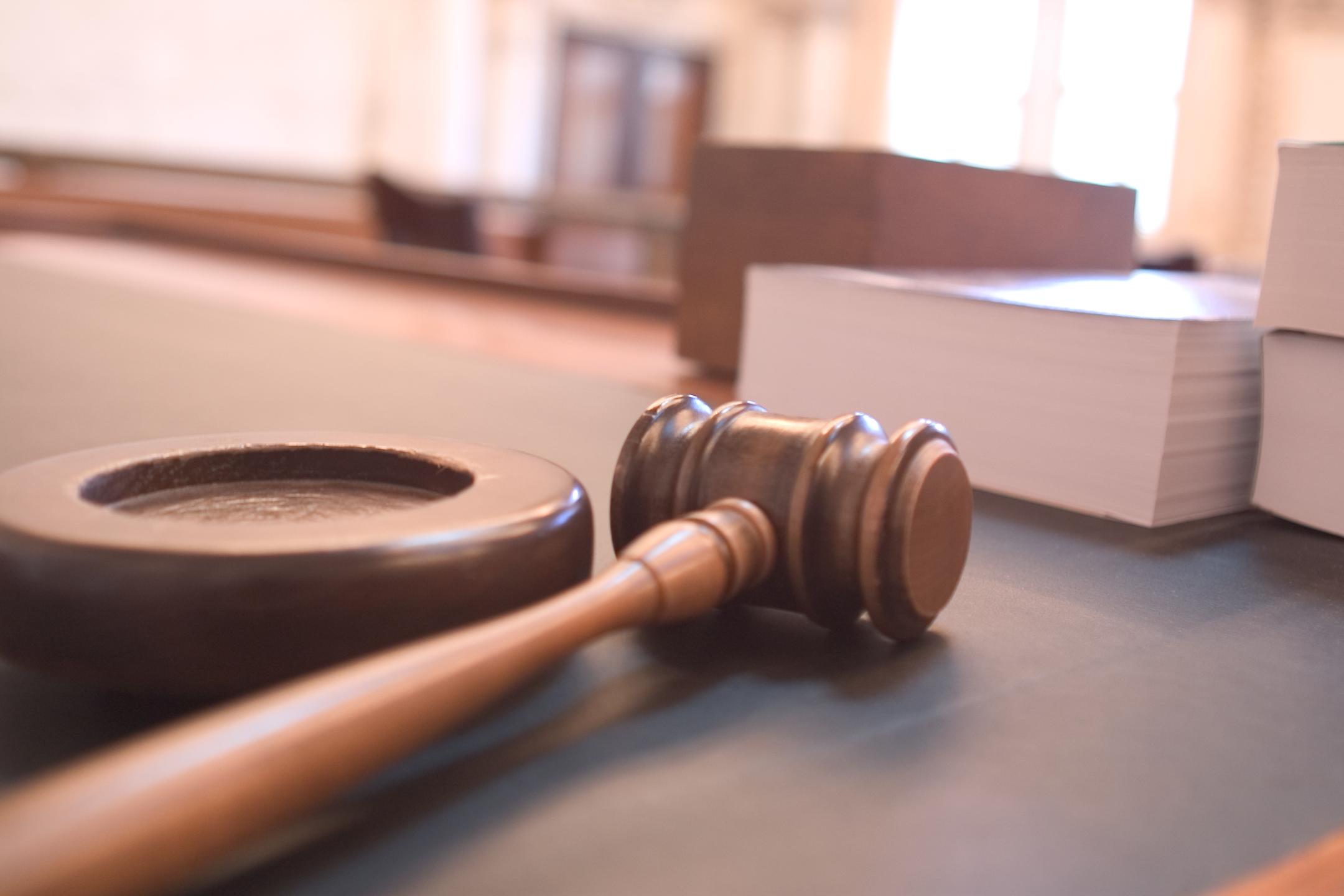 A wooden gavel resting on a block beside stacked documents on a polished desk