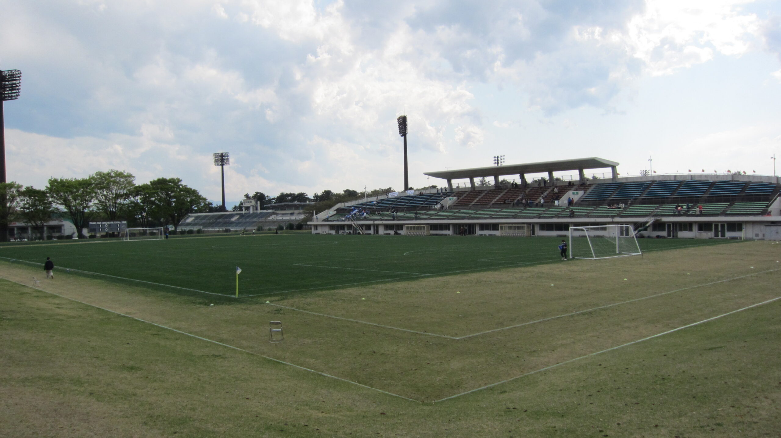 A football stadium lit by floodlights before an evening fixture with stands filling