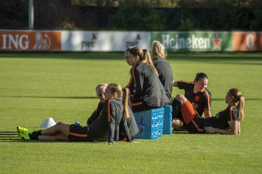 Players running sprint drills on a training pitch surrounded by hills