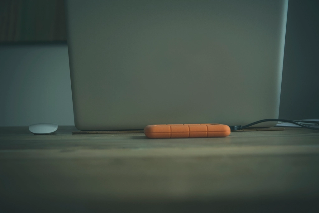 Several portable hard drives stacked on a desk beside a laptop and cables