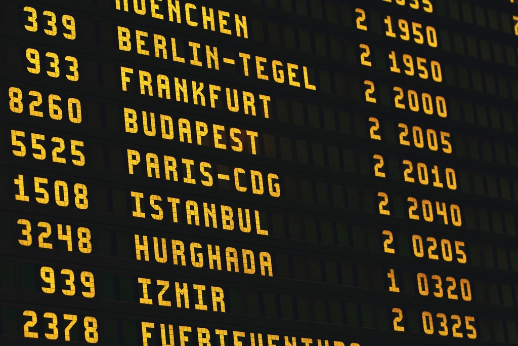 A departure board listing flights in an airport terminal with travellers passing beneath